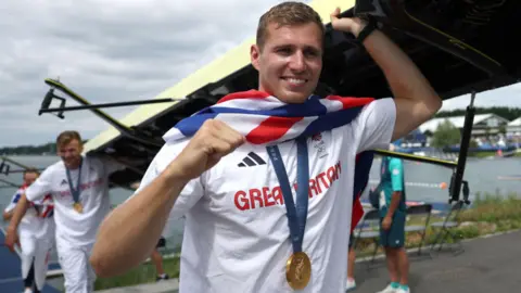 A man with the UK flag draped over his shoulders smiles with his fist in the air.