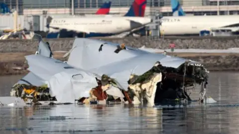 Getty Images The wreckage of the American Airlines plane in the Potomac River, with two parked aircraft visible in the background
