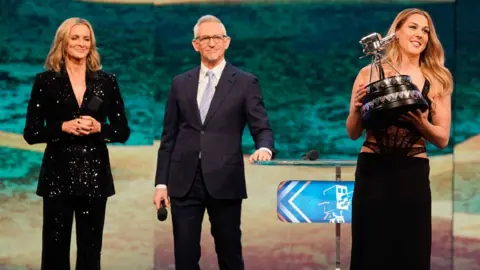 Gary Lineker and Gabby Logan watching on stage as Mary Earps holds her Sports Personality trophy