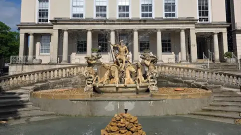 Visit Cheltenham The image is of Neptune's Fountain in Cheltenham. It is a monumental statuesque piece depicting Greek god Neptune in a shell-chariot, being drawn by four sea-horses and heralded by conch-shell blowing merman.