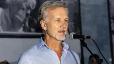 Getty Images Paul Lowe stands in front of a microphone giving a speech at a photography exhibition 