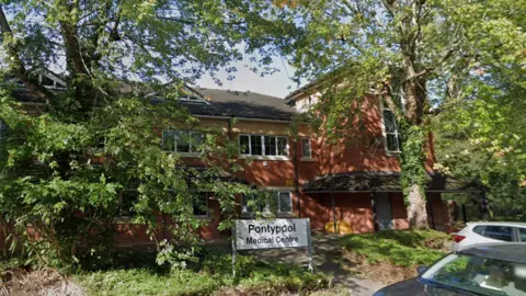 Google A two-storey brick building surrounded by several trees, with cars parked in front and a sign saying Pontypool Medical Centre.