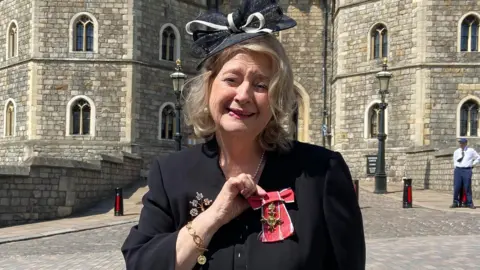 Wendy Daunt OBE standing outside Windsor Castle with her medal.