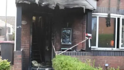 Crown Prosecution Service A house ravaged by fire. There is no front door and the doorframe and stairs are black with smoke and fire damage. 