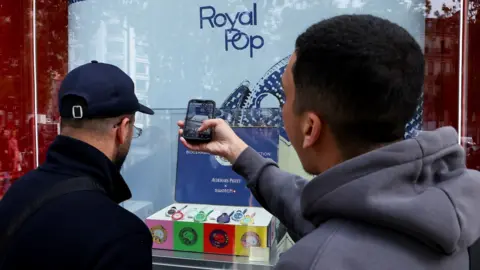People take photos through the window of the Swiss watch store Swatch to capture the new limited-edition 'Royal Pop' watches