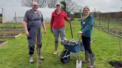 Growing Well Garden team are pictured planting trees. They are all wearing wellies and waterproof clothing.