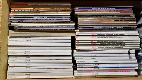 A close-up of shelves full of Vogue magazine, showing white the spines.