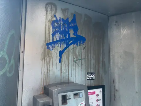 The inside of a phone box with dirty, graffiti-covered walls and a bashed up phone below.