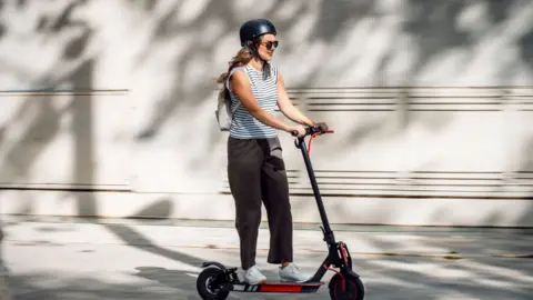 A woman riding an e-scooter wearing sunglasses and a helmet.