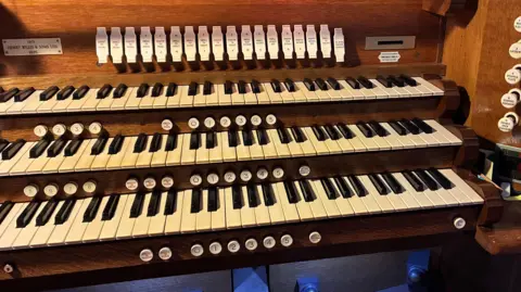 Sitting detached from the organ pipes and next to some church pews is the keyboard of the instrument.