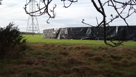 Supplied Plastic sheets surrounding a sink hole near an electricity pylon