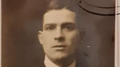 Family handout/PA Wire A sepia toned image of Frank Hills, he is looking directly at the camera, he wears a smart white collared shirt and has dark hair styled in a side parting