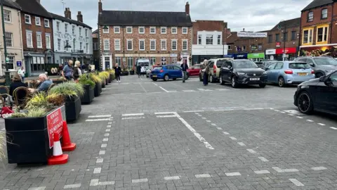 Natalie Bell/BBC New white road markings in foreground with people, parked cars and historic buildings in background