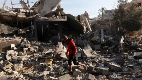 Reuters A Palestinian man walks over rubble following an Israeli air strike on a home in Nuseirat refugee camp, central Gaza (11 December 2024)