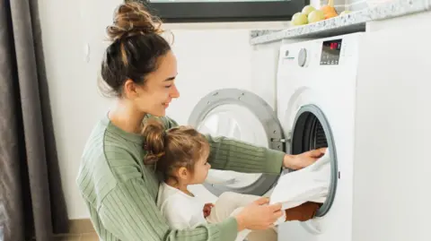 Getty Images Mother and child girl little helper loading washing machine