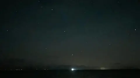 Millom Coastguard Rescue Team A dark stretch of sky with various bright white dots scattered across it. There is a light on the horizon.