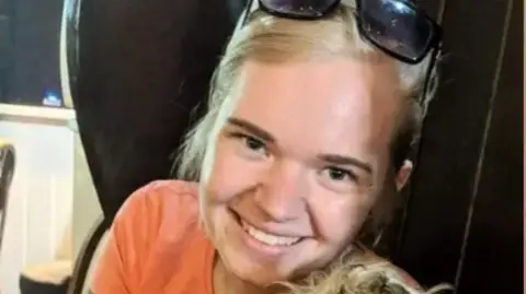 Family Handout Beth Matthews, with blonde hair and wearing an orange t-shirt, smiles at the camera