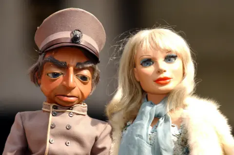 PA Parker and Lady Penelope successful  Thunderbirds - 2  puppets broadside  by side, Parker successful  a chauffeur's azygous   and Lady Penelope successful  bluish  sequins and fur