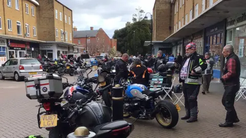 Westbury Court Care & Nursing Home Bikers wander about next to parked bikes. There are shops in the background.