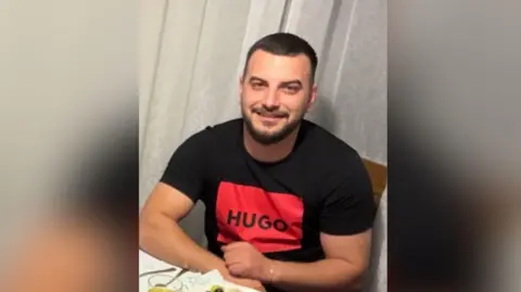 Ervin Lita wears a black t-shirt with a red "Hugo Boss" logo on the front.