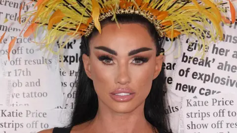 Katie Price wearing a headpiece made out of yellow and orange feathers. She is pouting at the camera while standing in front of a background of newspaper extracts.