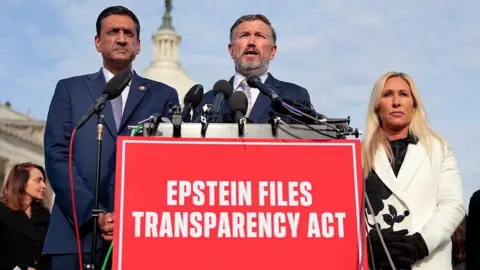 Getty Images Representatives Ro Khanna, Thomas Massie and Marjorie Taylor Greene speak behind a red sign that reads "Epstein Files Transparency Act"
