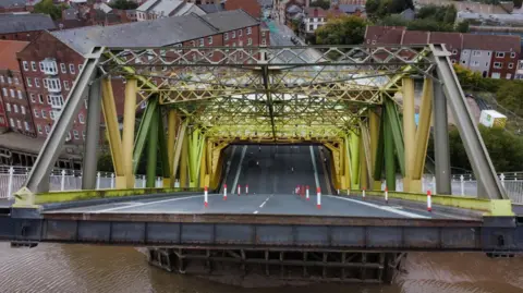 Hull City Council Aerial view of Drypool Bridge which has a yellow metal lifting mechanism and brick control room at one end spanning the roadway.