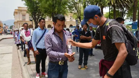 AFP A worker sanitises people's hands as they queue for an allowance from the local government