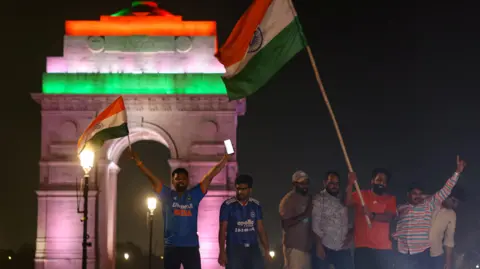 Reuters A group of men - with two of them holding Indian flags - celebrate India's T20 World Cup victory near Delhi's India Gate on Sunday night.