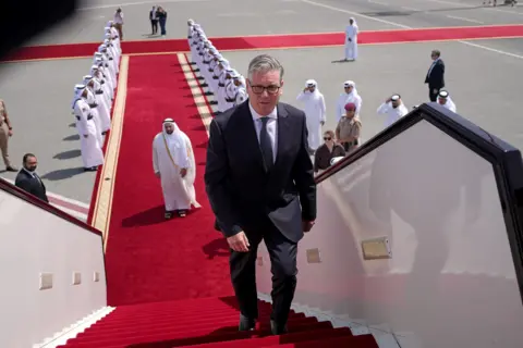 PA Media Keir Starmer boarding a plane at the airport in Doha, Qatar. There is a red carpet, lined with men, leading up to the plane