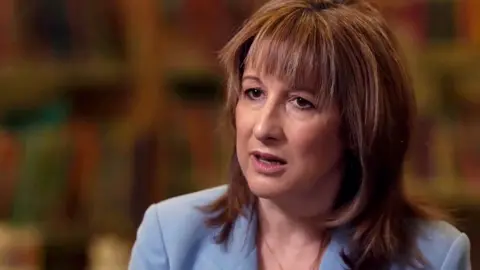 Chancellor Rachel Reeves, sitting down being interviewed, wearing a light blue suit jacket