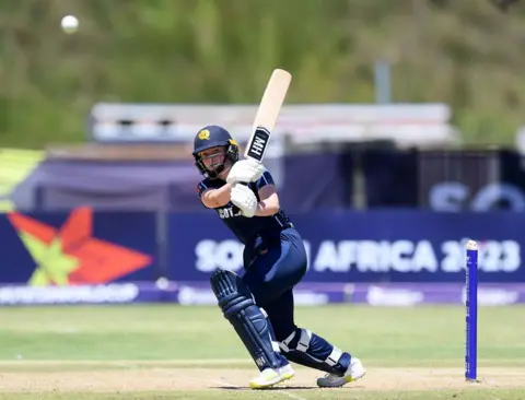 Getty Images Niamh Muir in a dark blue cricket outfit plays a driving shot with her bat before setting off for a run