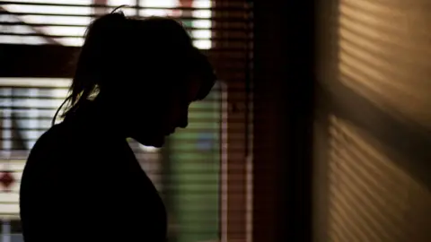 Getty Images Woman in shadow standing in front of window blinds