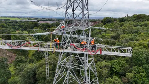 BBC Engineers on an overhead platform work on an electricity pylon tower in Airdrie, North Lanarkshire in Scotland. July 2025 (photo by Morgan Spence).