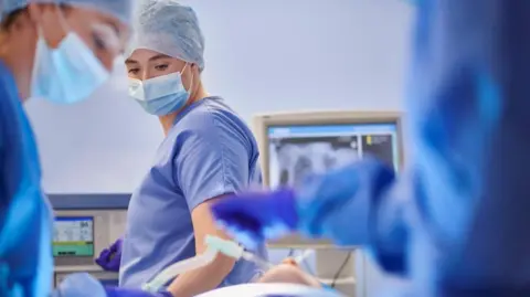 Woman health care staffer operating a machine during an operation in a hospital theatre.