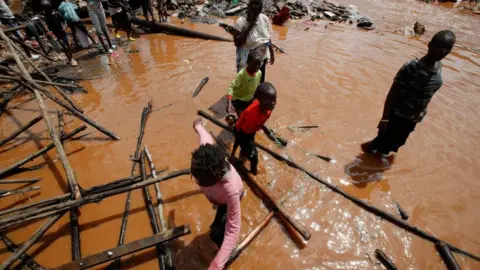 Reuters Residents wade through flood waters after the Nairobi river burst its banks and destroyed their homes within the Mathare valley settlement in Nairobi, Kenya April 24, 2024