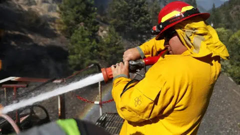 A firefighter assigned to the Union Pacific Fire Train sprays water on to the tracks to hinder the Dixie Fire in Plumas National Forest, California, on 17 July 2021