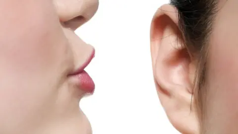 Getty Images Someone whispering in someone else's ear
