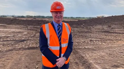 A man in an orange hard hat and orange high visibility jacket on a building site.