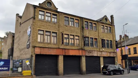 A stone three storey building with a series of garage doors on the ground floor level with black shutters