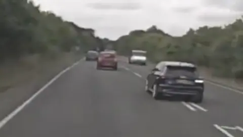 A speeding black Ford Focus can be seen speeding and overtaking traffic on the road at Clacton