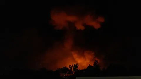 A plume of smoke rises in the dark