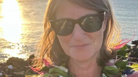 A woman with sunglasses stands in front of the sea 