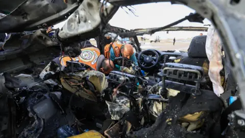 Reuters Palestinians inspect the site of an Israeli strike on a car in Gaza City, December 13 2025