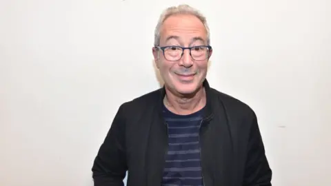 man standing against white wall wearing glasses and striped t-shirt