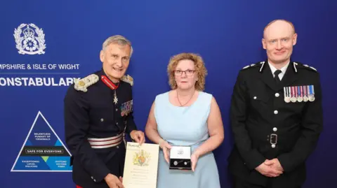 Hampshire Constabulary A woman dressed in blue receives an award from the Lord-Lieutenant of Hampshire and Hampshire & Isle of Wight Chief Constable