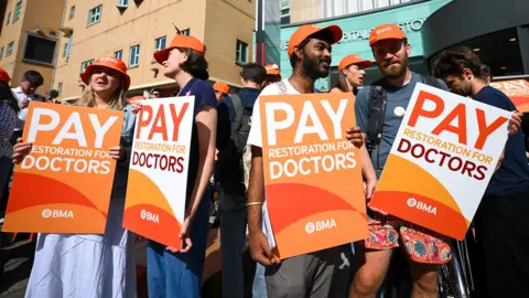 Resident doctors on strike hold orange placards saying 'pay restoration for doctors' with the BMA logo on them outside Bristol Royal Infirmary on Friday.