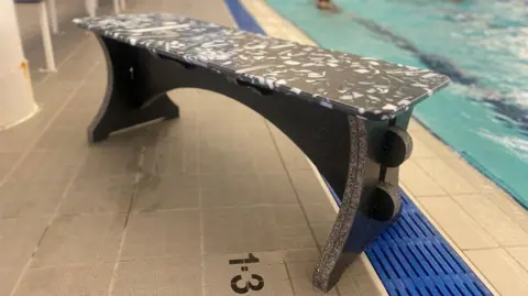 A grey bench by the side of a pool