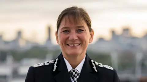 A close up of Dame Lynne who is smiling, She has brown hair and is wearing the uniform of a senior police officer. 