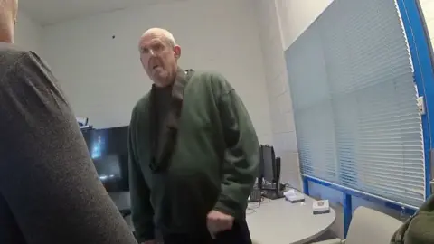 Old man with short white hair in a green jumper.